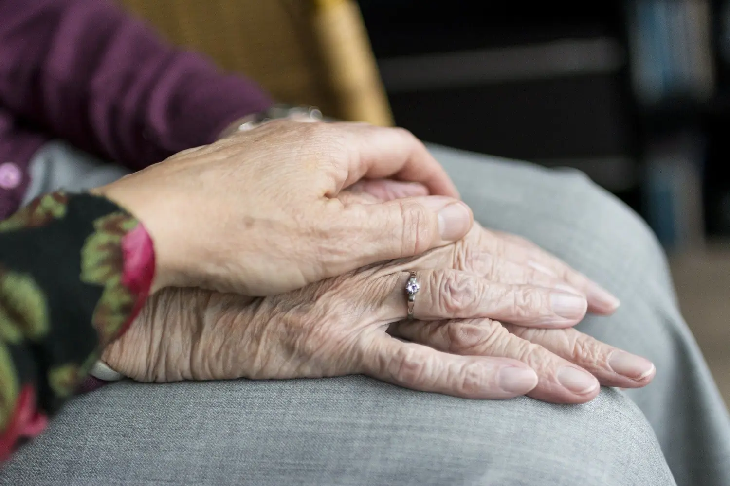 Pflegeteam mit Hand und Herz, 2 alte Menschen halten sich zum Trost an den Händen